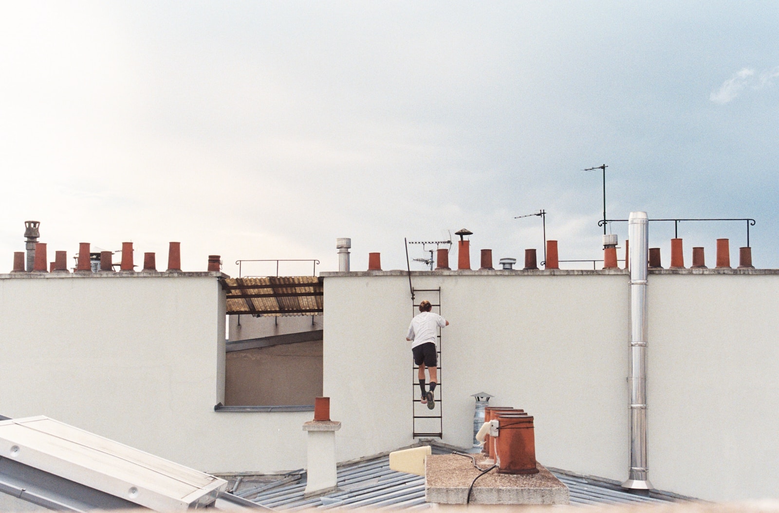 man in white t-shirt and black pants standing on white concrete building during daytime